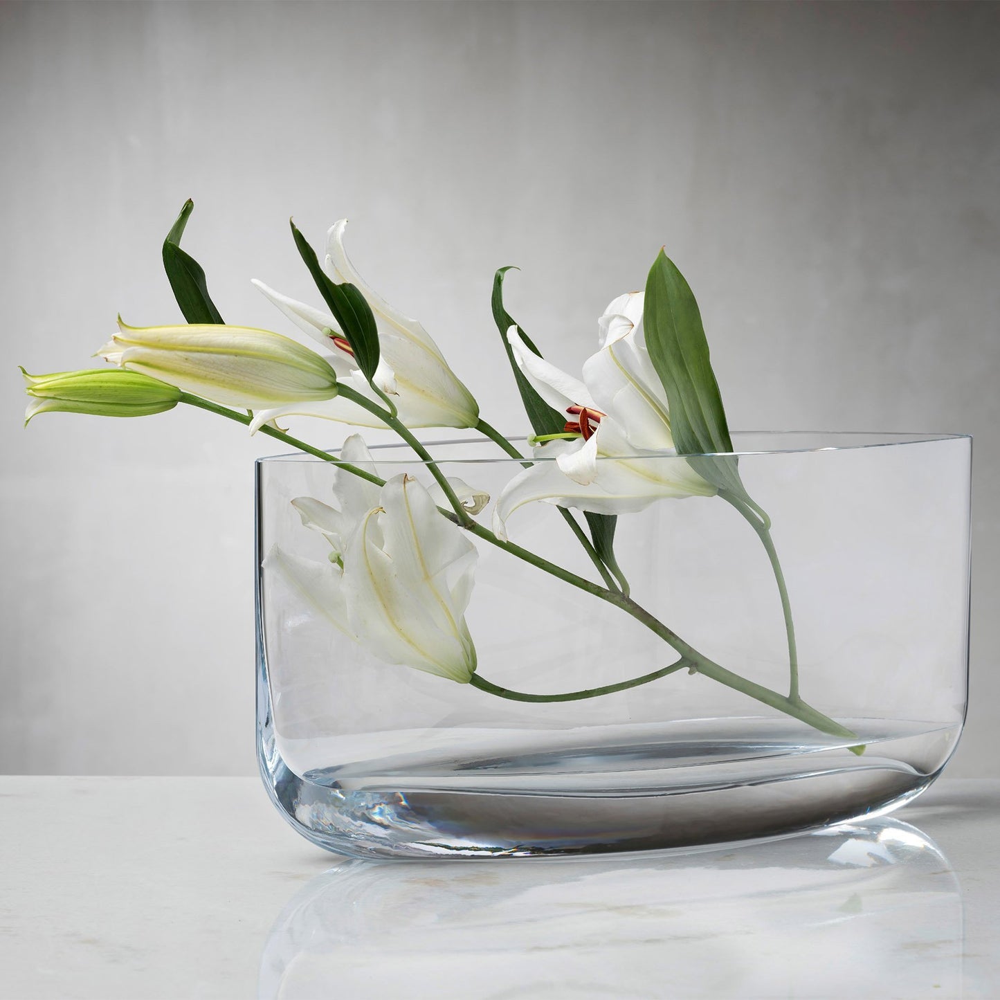 Clear wide-mouth vase with lilies diagonally resting on tip.