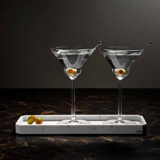 Two dirty martinis on a marble tray against dark background.